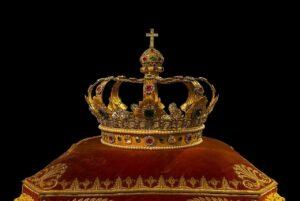 A golden king's crown on a red cushion.