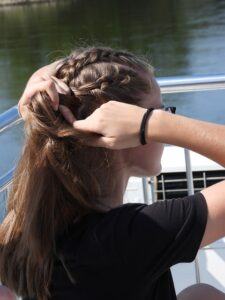 A girl tying her hair in a French braid.