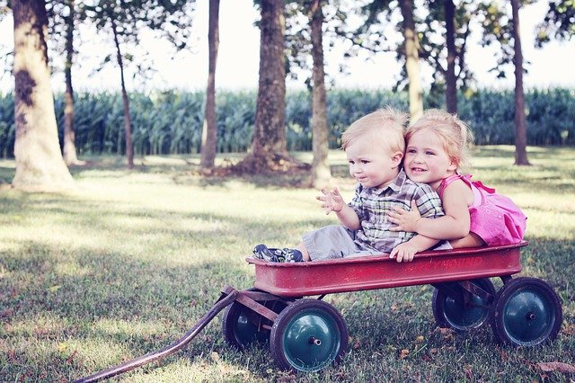 A boy and a girl riding a red wagon.