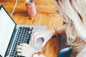 Blonde woman using a laptop and drinking soda.