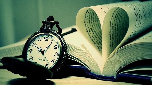 A pocket watch next to a book with two pages shaped like a heart.