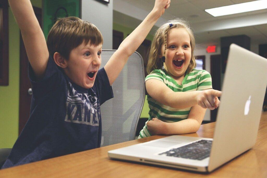 Two kids smiling in front of a computer.