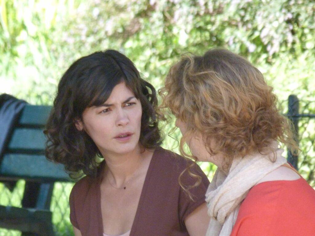 A young brunette woman wearing an indigo blouse and talking to another woman.