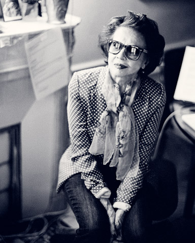 Black and white photo of an old woman wearing a suit and glasses.