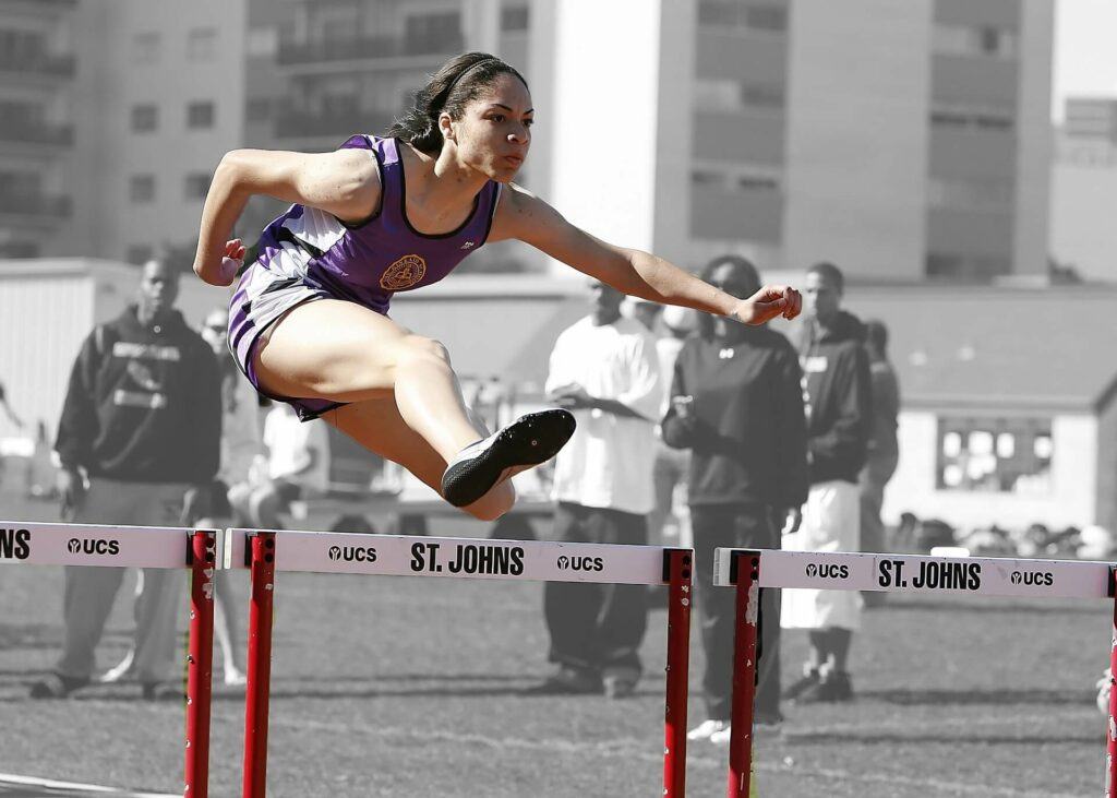 A female athlete jumping over some obstacles.