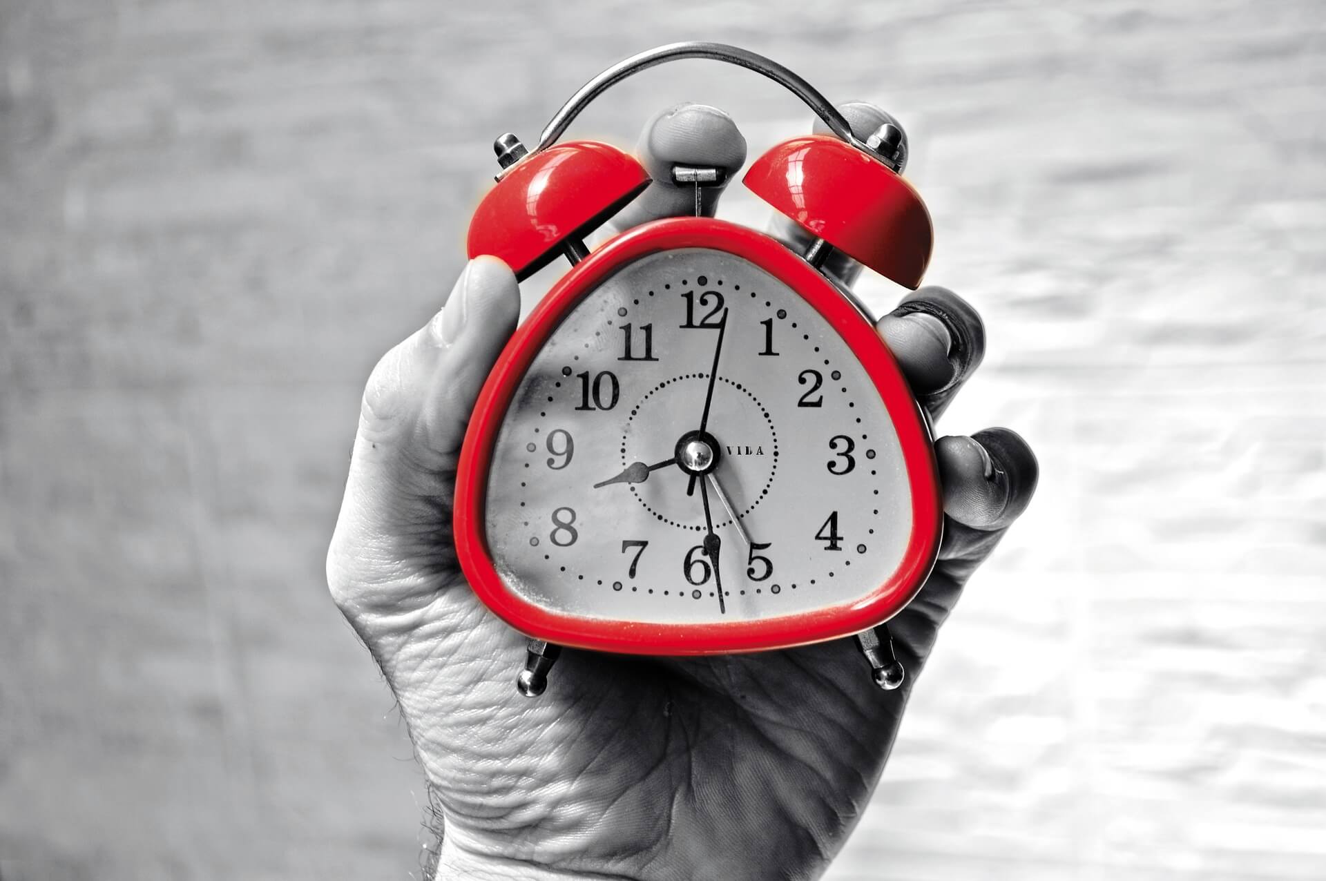 A hand holding a red alarm clock.